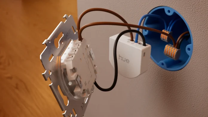 Een witte Philips Hue wandschakelaar module aangesloten op de elektrische bedrading van een lichtschakelaar bij een blauwe inbouwdoos.