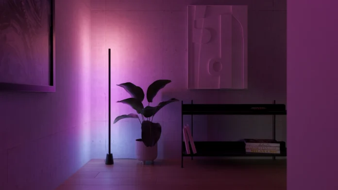Een moderne kamer met een slanke staande lamp die een sfeervolle paarse hue op de betonlook muur en een kamerplant werpt.