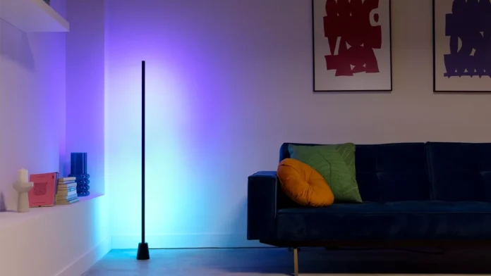Een slanke Wiz vloerlamp verlicht een moderne woonkamer met een sfeervolle paarse en blauwe gloed naast een donkerblauwe bank.