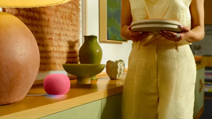 Een roze Google Home Speaker met Gemini AI staat op een houten dressoir in een sfeervol interieur terwijl een persoon borden vasthoudt.