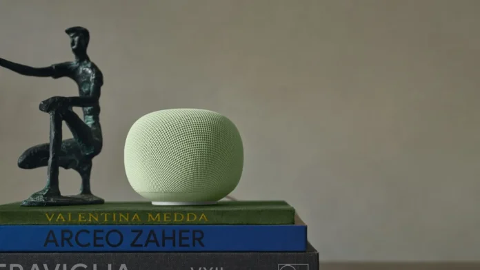 Een lichtgroene Google Home Speaker met Gemini AI staat op een stapel boeken naast een abstract bronzen beeld tegen een neutrale achtergrond.
