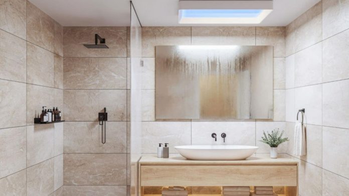 Moderne badkamer met beige marmerlook tegels, een licht houten wastafelmeubel en een Philips Skylight aan het plafond die een helderblauwe gloed verspreidt.