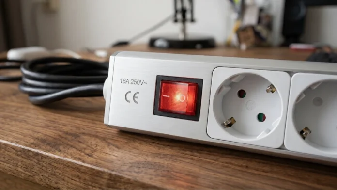 Zilveren stekkerdoos met een verlichte rode aan-uitknop op een houten bureau, zet deze stekkerdoos uit bij onweer blikseminslag.