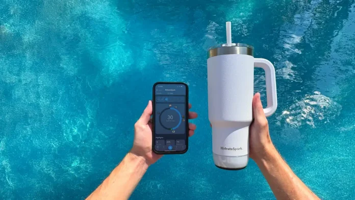 Een persoon houdt een witte HidrateSpark drinkbeker en een smartphone met een hydratatie-app vast boven het glinsterende blauwe Water van een zwembad.