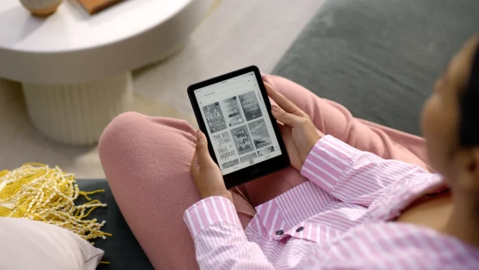 Een persoon in roze kleding zit op de bank en bekijkt een digitale bibliotheek op een Kindle, wat helpt bij de juiste e-reader kiezen voor optimaal leesplezier.