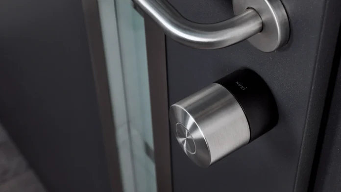 Een modern roestvrijstalen Nuki Smart Lock geïnstalleerd op een antracietgrijze deur biedt een helder overzicht voor wie verschillende modellen van de Nuki Smart Lock vergelijken wil.