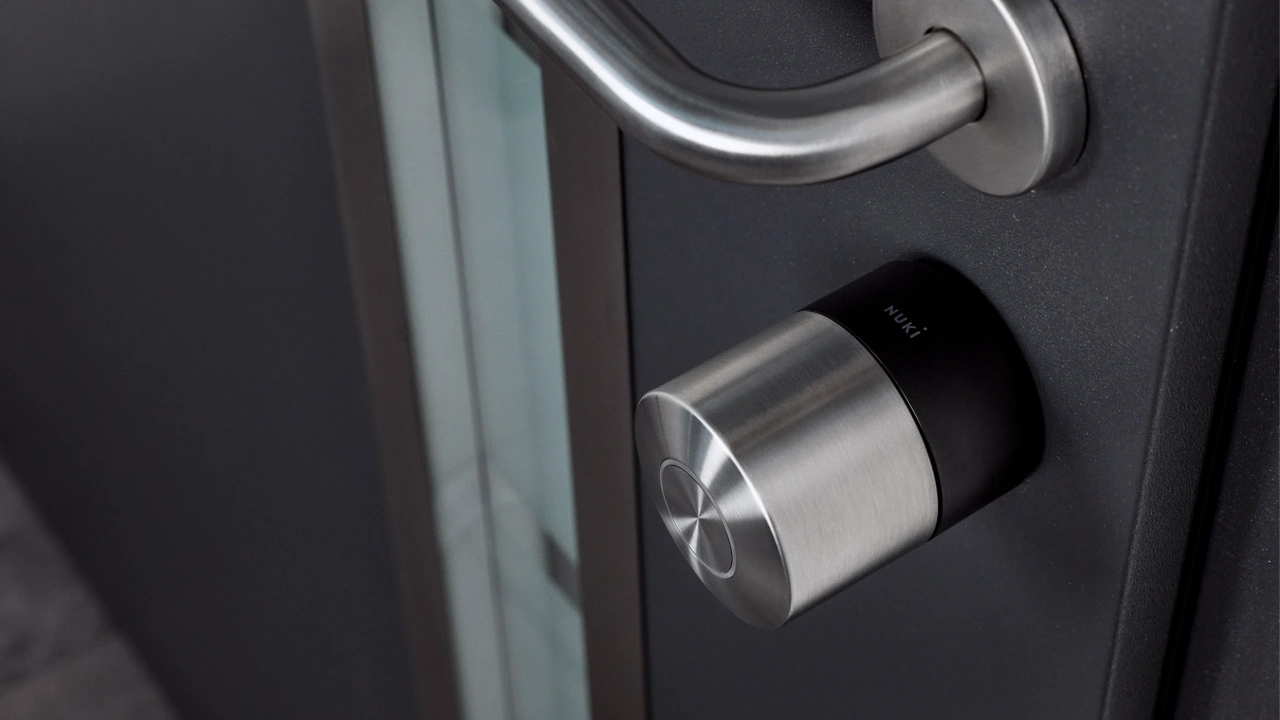 Een modern roestvrijstalen Nuki Smart Lock geïnstalleerd op een antracietgrijze deur biedt een helder overzicht voor wie verschillende modellen van de Nuki Smart Lock vergelijken wil.