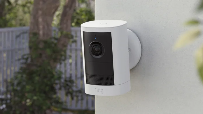 Een van de Ring 2K camera's is gemonteerd aan een witte buitenmuur met uitzicht op een groene tuin en een schutting.