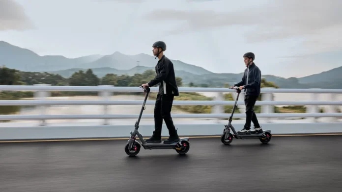 Twee mannen met helmen rijden op hun segway elektrische steps over een brug met een schilderachtig uitzicht op bergen en water.