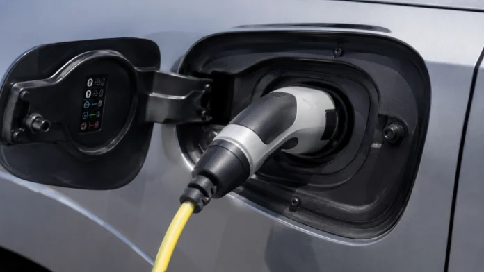 Close-up van een grijze elektrische auto die wordt opgeladen met een geel snoer, ideaal voor wie gebruikmaakt van de Slim laden Gelderland korting.