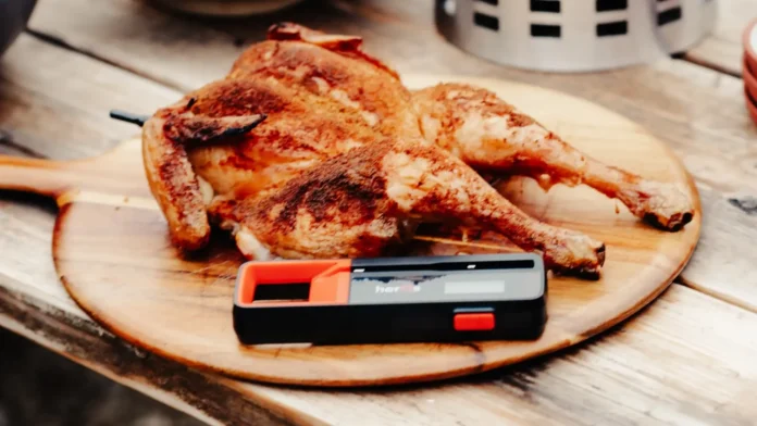 Een goudbruin gebraden hele kip op een houten serveerplank gepresenteerd met een slimme vleesthermometer voor een perfecte garing.