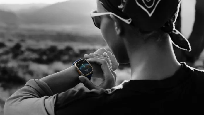 Een wandelaar in een ruig berglandschap bekijkt de satellietfuncties op een robuuste Apple Watch Ultra om de pols.