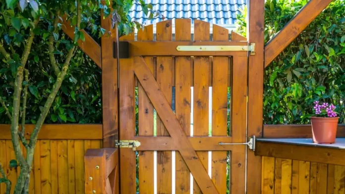 Een klassieke houten tuinpoort in een groene tuin waar een buitensensor zorgt voor automatische verlichting bij de ingang.