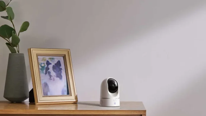 eufy beveiligingscamera voor binnen op een houten tafel naast een fotolijstje en plant.