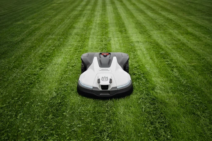Een witte Husqvarna robotmaaier rijdt over een strak gemaaid groen gazon met duidelijke banen.
