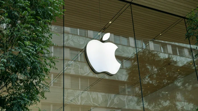 Verlicht Apple logo op een glazen winkelpui met reflecties van gebouwen en groene planten.