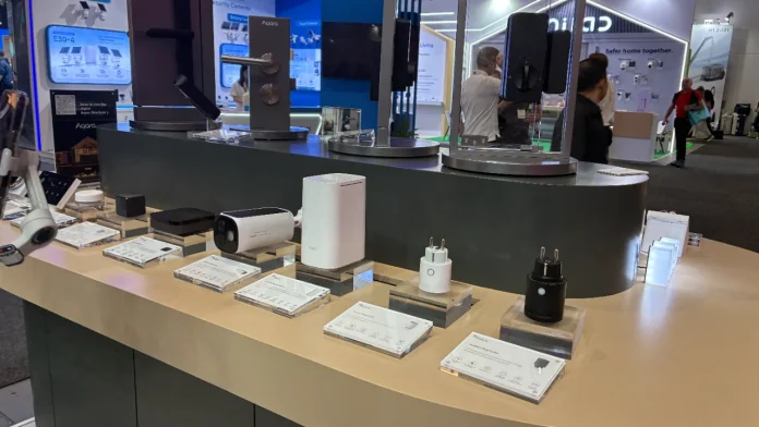 Aqara smart home devices including security cameras, hubs, and smart plugs on display at a technology trade show.
