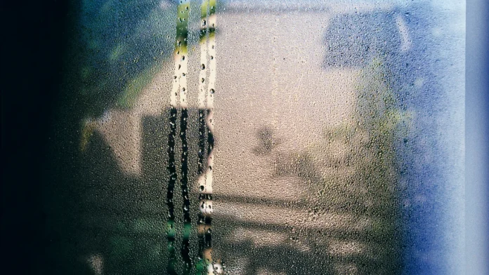 Condensation op een beslagen raam met waterdruppels en een wazige achtergrond.