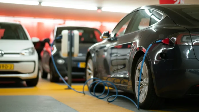 Dark grey EV plugged into a charging station in an indoor parking garage.