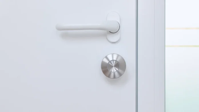 Zilveren Nuki smart lock op een witte deur met een witte deurklink.