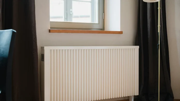 Witte moderne radiator onder een houten vensterbank in een kamer met donkere gordijnen.