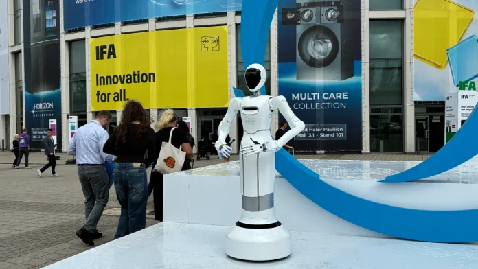 White humanoid robot at IFA Berlin tech show with innovation banners and people in the background.