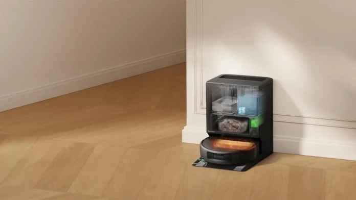 Roomba robot vacuum at its transparent self-emptying base station showing internal tanks on a wooden floor.