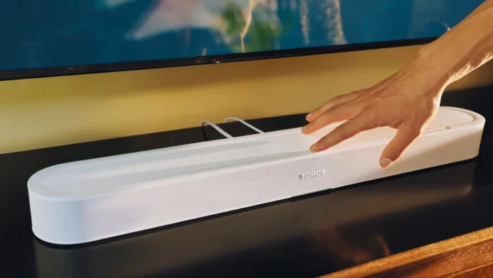 Witte Sonos soundbar op een zwart tv-meubel terwijl een hand de touch-bediening gebruikt.