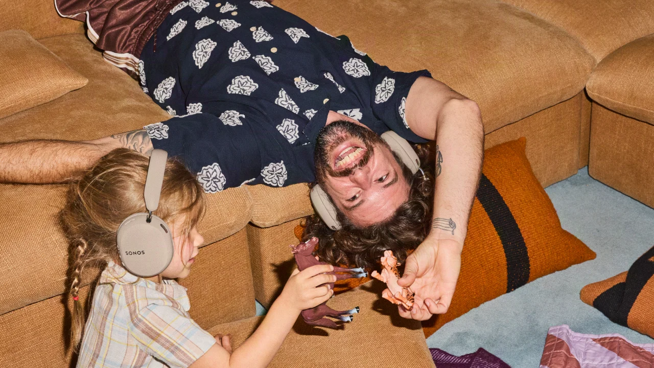 Man and child wearing sONOS headphones while playing with toy animals on a couch.