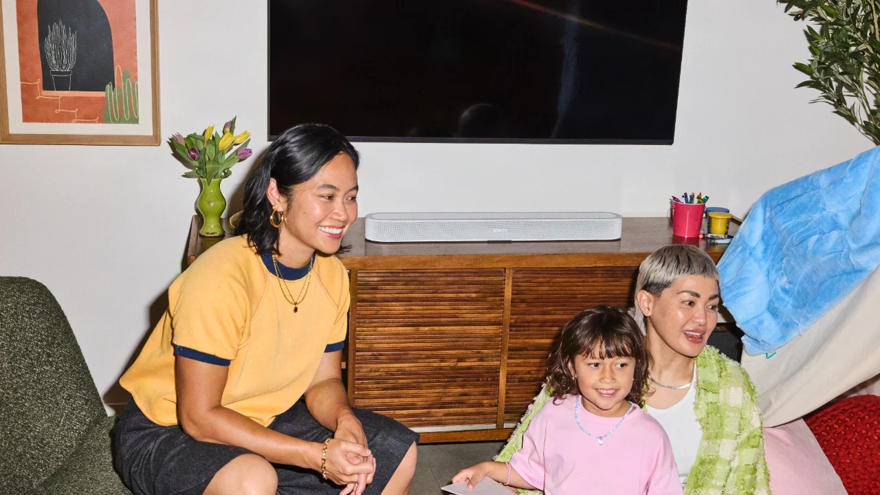 Family in a living room with a white Sonos soundbar on a wooden media console below a TV.