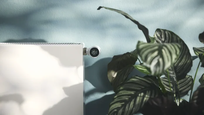 tado slimme radiatorknop op een witte radiator naast een groene kamerplant.