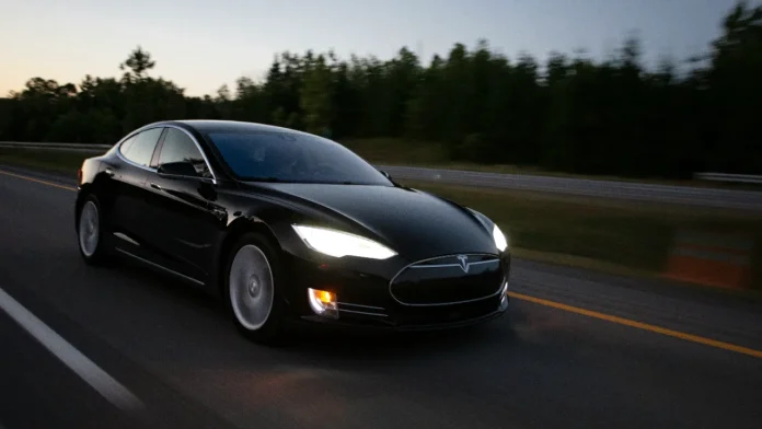Zwarte Tesla Model S rijdt op de snelweg tijdens de schemering met koplampen aan.