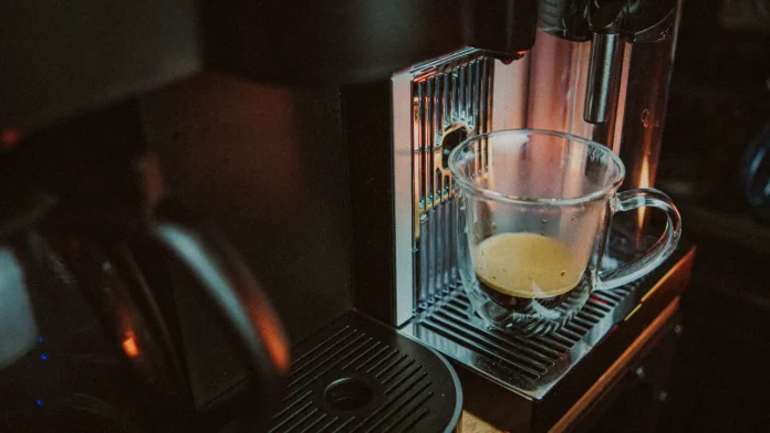 A glass mug of espresso coffee with rich crema sitting on a modern coffee machine.