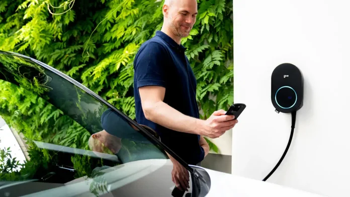 Man controleert zijn laadsessie in een app naast een elektrische auto aan een wandlader