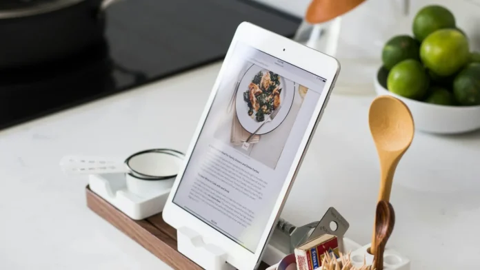 Een iPad op een houten standaard op een keukenblad, naast een houten lepel en limoenen
