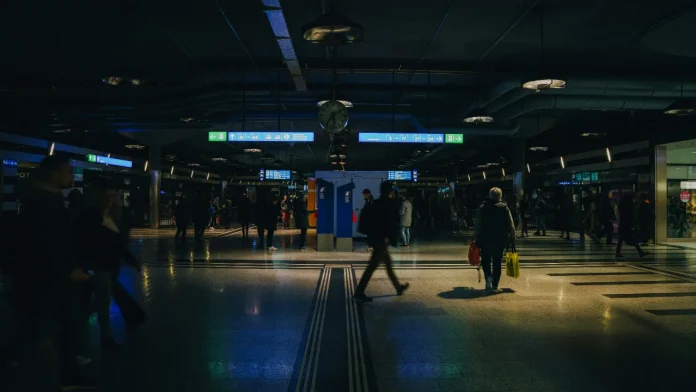 Sfeervol licht in een donker treinstation met reizigers en verlichte informatieborden.