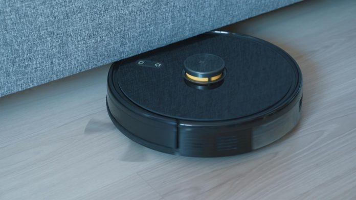 Zwarte robotstofzuiger rijdt onder een bank over een houten vloer