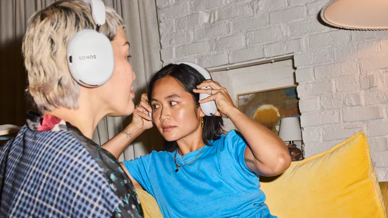 Twee vrouwen dragen witte Sonos over-ear koptelefoons in een sfeervolle woonkamer.