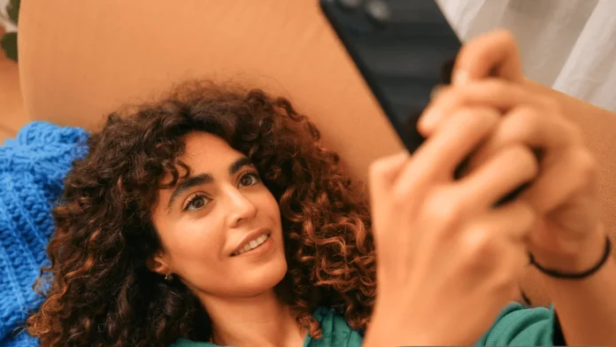 tado AI Assist in de app: een lachende vrouw op de bank kijkt op haar telefoon