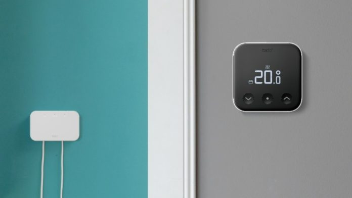 Witte verwarmingsketel en tado Bridge met kabels op turquoise muur, naast een zwarte tado slimme thermostaat (20.0°) op grijze muur met houten plank.